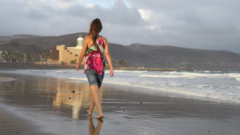 Cinematic-shot-of-a-woman-walking-and-admiring-the-Alfredo-Kraus-auditorium-from-Las-Canteras-beach,-on-the-island-of-Gran-Canaria
