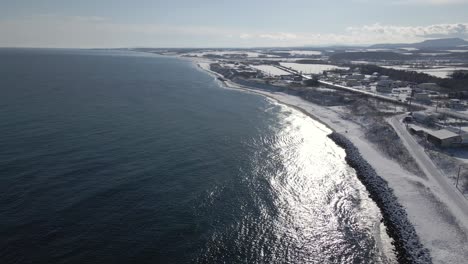 Drone-flying-along-coastline-of-Japan-in-winter-with-snow-and-town