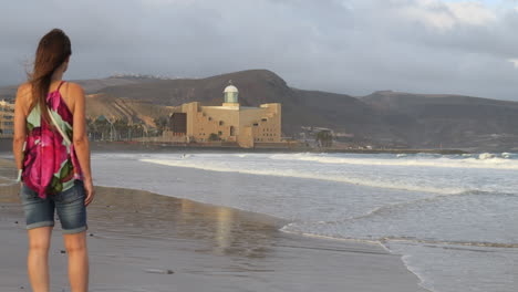 Cinematic-shot-of-a-woman-admiring-the-Alfredo-Kraus-auditorium-while-the-waves-break-on-the-shore-of-Las-Canteras-beach,-on-the-island-of-Gran-Canaria