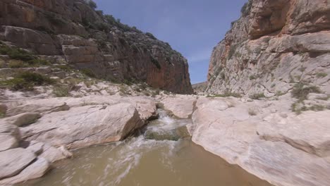 Low-first-person-view-aerial-up-shallow-river-in-narrow-rock-gorge