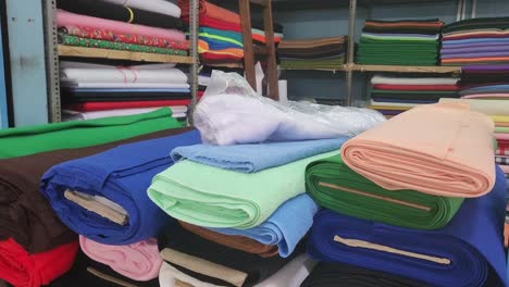 4k-video-of-many-sheets-of-different-colored-fabric-stacked-up-on-top-a-counter-and-more-cloth-in-racks-behind-it