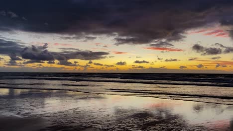 Dramatic-and-cinematic-purple-and-yellow-sunrise-sunset-over-a-calm-pacific-ocean-beach-scene-with-the-smooth-wet-sands-giving-sensational-reflections-of-the-vivid-sky-above