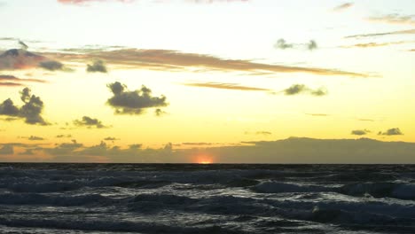 Serene-sunrise-over-the-rolling-waves-of-the-pacific-ocean-with-a-bright-yellow-and-orange-sky