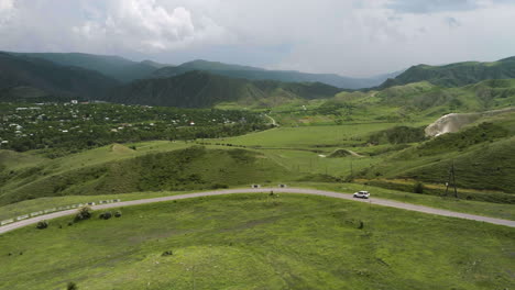 White-SUV-Car-Driving-On-The-Road-With-Panoramic-View-Of-Green-Grassland-And-Mountain-In-Summer-In-Georgia