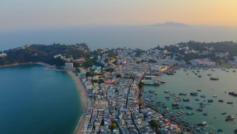 Drone-shot-traveling-forward-above-a-city-built-on-an-isthmus-with-an-harbor-and-a-popular-beach-during-golden-hour