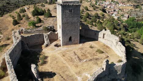 Backward-flight-view-of-a-medieval-tower-in-a-castle-in-Ucero,-Soria-,-surrounded-by-walls,-in-the-top-of-a-hill