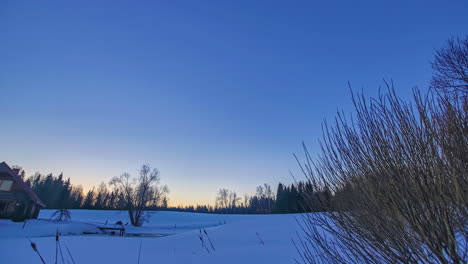 Timelapse-shot-of-beautiful-sunrise-over-wooden-cottage-along-blue-sky-during-cold-winter-day-with-snowy-field