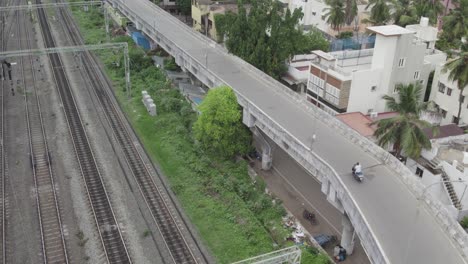 Aerial-shot-of-a-biker-going-on-a-bridge-near-a-railway-track-surrounded-by-buildings-and-trees