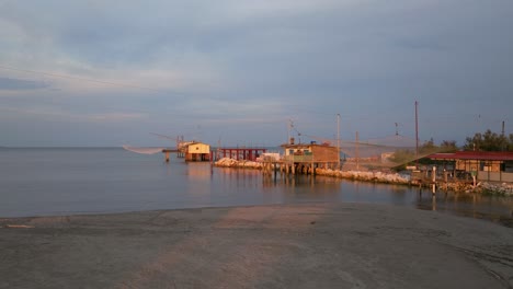 Luftaufnahme-Von-Fischerhütten-Am-Ufer-Der-Mündung-Bei-Sonnenuntergang,-Italienische-Fischermaschine,-Genannt-&quot