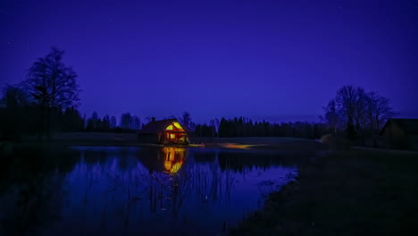 Static-shot-from-evening-to-night-sky-star-movement-in-timelapse-in-rural-countryside-with-the-view-of-a-lake-in-front-of-small-cottage