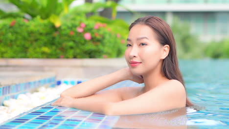 An-attractive-young-woman-in-a-swimming-pool-leans-up-along-the-edge-of-a-posh-resort-swimming-pool