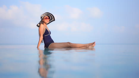 Profile-of-a-healthy-young-woman-sitting-on-the-edge-of-an-infinity-pool-against-a-blue-ocean-horizon