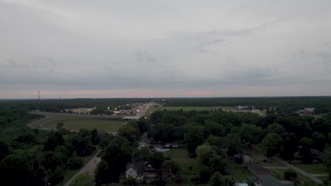 Aerial-drone-shot-over-small-town-homes-on-both-sides-of-a-road,-set-among-dense-vegetation-at-sunset
