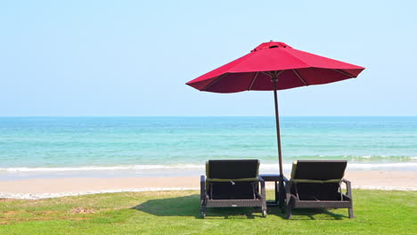Two-empty-chaise-lounge-chairs-sitting-under-a-shade-umbrella-facing-the-incoming-tide