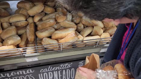 Video-Von-Einer-Person-In-Einer-Bäckerei,-Die-Aus-Einem-Großen-Stapel-Brote-Heraussucht-Und-Sie-In-Eine-Tüte-Legt