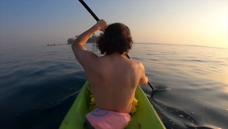 Joven-Remando-En-Un-Kayak-En-El-Océano-Con-Una-Isla-Como-Fondo