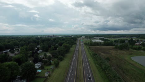 A-busy-highway-is-captured-by-a-drone,-and-numerous-houses-in-the-town-can-be-seen-next-to-the-highway