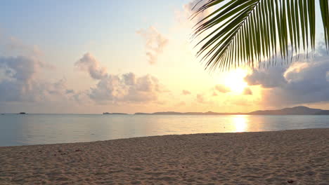 Pfanne-Eines-Tropischen-Sandstrandes,-Umrahmt-Von-Einem-Farbenprächtigen-Sonnenuntergang-Und-Palmwedeln