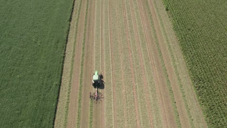 On-a-farm-field-in-southwest-Wisconsin,-a-farmer-rakes-hay-using-a-rotary-hay-rake