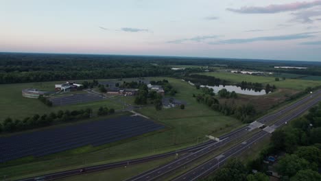 Drone-footage-of-the-solar-panels-installed-on-the-side-of-the-road-while-numerous-vehicles-is-passing-by-and-the-highway-is-surrounded-by-trees-and-greenery