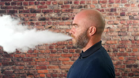 Side-portrait-of-a-man-vaping-indoors-in-front-of-a-brick-wall-with-cloud-of-smoke