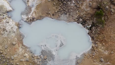 Ascending-top-down-flight-over-geothermal-mudpot-with-rising-fumes-in-Iceland