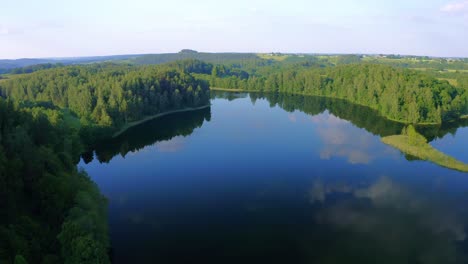 Aerial-view-of-a-calm-lake-reflecting-the-sky-surrounded-by-forest-in-Poland