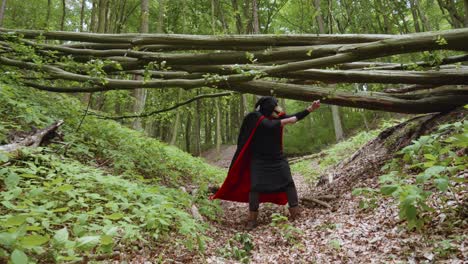 Grim-Reaper-In-Black-Hooded-Cloak-Dancing-In-The-Woods-Under-The-Trunk-Of-A-Fallen-Tree
