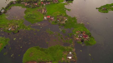 Drone-flying-forwards-revealing-several-humble-houses-on-lawns-surrounded-by-water-after-flooding