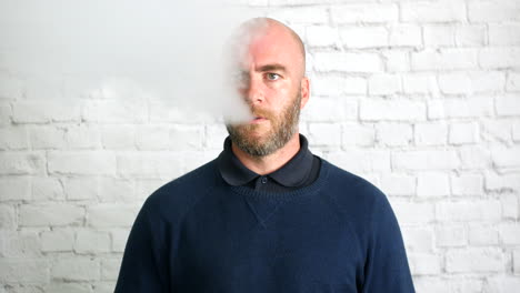 Porträt-Eines-Mannes,-Der-Drinnen-Vor-Einer-Weißen-Wand-Mit-Rauchwolke-Dampf-Macht