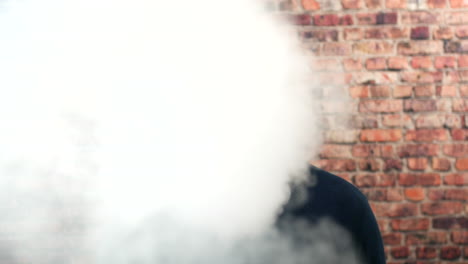 Portrait-of-a-man-vaping-indoors-in-front-of-a-brick-wall-with-cloud-of-smoke