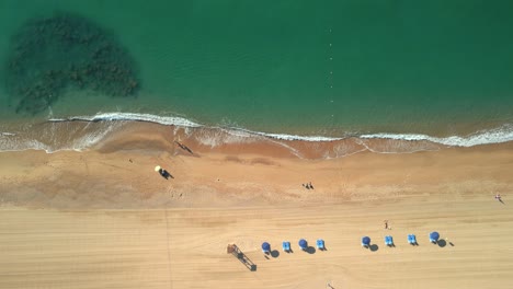 Luftaufnahme-über-Einem-Strand-Mit-Gelbem-Sand-Und-Transparentem-Türkisfarbenem-Wasser-In-Malgrat-De-Mar,-Provinz-Barcelona-Flug-über-Hängematten-Und-Liegestühle-1
