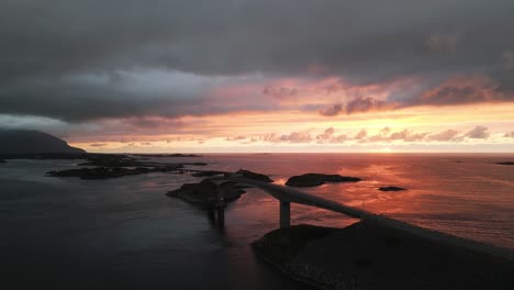 Fliegen-über-Die-Atlantic-Ocean-Road-In-Norwegen-Bei-Sonnenuntergang-Mit-Der-Architektonischen-Meisterwerkbrücke,-Umgeben-Vom-Ozean-Und-Autos,-Die-Die-Inseln-überqueren