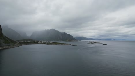 Rising-cinematic-movement-showing-the-mountainous-norwegian-landscape-on-the-lofoten-with-a-view-of-reine-with-fog,-mountains-fjord-and-sea-in-the-background