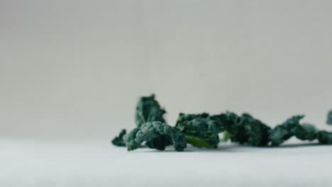 Pieces-of-green-kale-leaves-fall-in-slow-motion-onto-a-white-surface