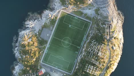 Rotating-upwards-aerial-footage-showing-the-football-soccer-stadium-in-Henningsvaer,-Lofoten,-Norway-with-its-classic-view-on-an-island-right-by-the-ocean-and-surrounded-by-tall-mountains