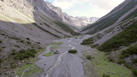 Aerial-drone-footage-slowly-twisting-and-descending-in-a-dramatic-glacial-valley-surrounded-by-a-steep-mountains-and-pine-trees-with-patches-of-snow-and-an-alpine-river-in-Switzerland