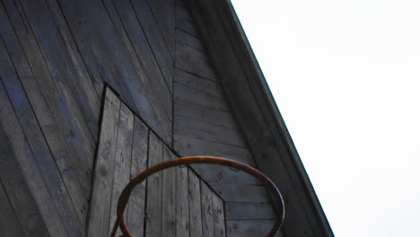 Old-rusty-wooden-house-with-a-basketball-net-in-a-cloudy-back-in-the-backyard