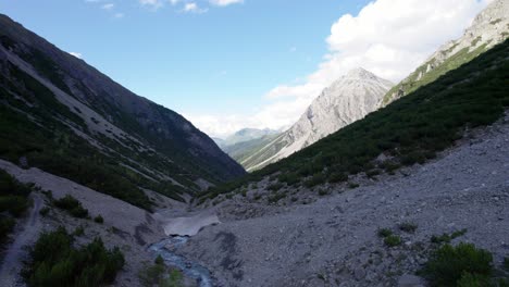 Aerial-drone-footage-slowly-rising-from-a-glacial-valley-floor-surrounded-by-a-steep-mountains-and-pine-tree-covered-slopes-with-patches-of-snow-and-an-alpine-river-in-Switzerland