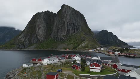Flying-across-the-classical-traditional-fisher-village-of-Hamnoy-in-Lofoten,-Norway-with-classic-red-rorbuer-huts-cottages-with-a-view-towards-the-iconic-mountain-and-the-ocean