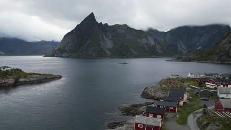 Flying-over-iconic-Hamnoy-fisher-village-in-Norway,-Lofoten-with-a-view-towards-the-mountains-and-ocean-with-seagull-flying-below-the-camera-and-above-the-ocean