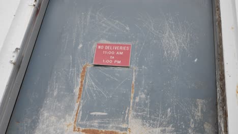 Slow-Motion-Pull-Out-from-a-Creepy-Red-No-Deliveries-Sign-On-an-Abandoned-Warehouse-Door