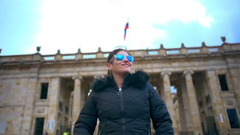 Medium-shot-of-A-woman-dressed-with-black-jacket-and-blue-sunglasses-stare-at-the-Government-Palace-in-Bogotá-in-a-sunny-afternoon-1