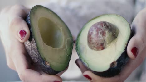 Detail-of-an-avocado-being-held-by-a-girl-with-red-nail-polish:-she-opens-the-avocado-in-two-and-shows-the-inside-with-the-pit