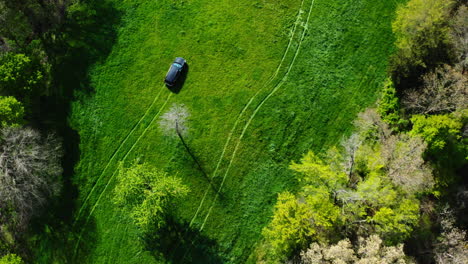 Aerial-View-Of-Car-Driving-On-The-Green-Grassy-Field-Leaving-Tire-Tracks