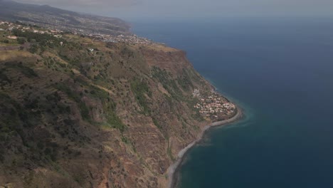 Aerial-view-of-the-calheta-parish-in-the-south-coast-of-Madeira-island,-drone-moving-to-the-right-showing-the-blue-ocean-and-the-green-hills-of-madeira-island
