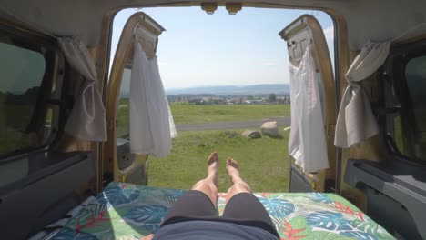 Static-close-up-of-a-woman-lying-on-the-mattress-of-a-camper-van-overlooking-a-green-landscape