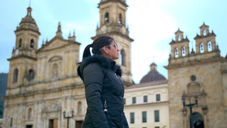 Medium-shot-of-A-woman-dressed-with-black-jacket-and-blue-sunglasses-stare-at-the-Government-Palace-in-Bogotá-in-a-sunny-afternoon
