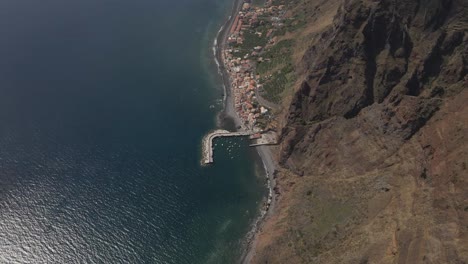 Vista-Aérea-De-La-Parroquia-Calheta-En-La-Isla-De-Madeira,-Drone-Avanzando-Mostrando-El-Contraste-Entre-El-Pueblo-Cerca-Del-Mar-Y-Las-Montañas-En-El-Fondo