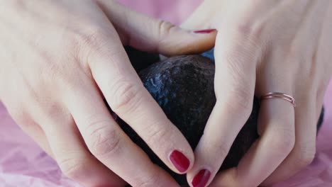 Three-avocados-are-placed-on-a-pink-fabric,-two-girl-hands-come-in-and-take-one-very-gently,-slow-motion-scene-and-natural-light